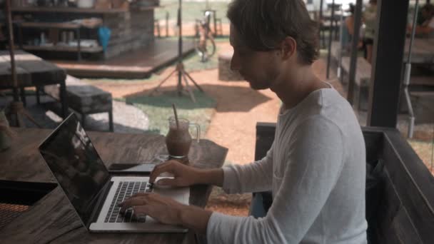 Jovem freelancer trabalhando em um computador portátil no café ao ar livre — Vídeo de Stock