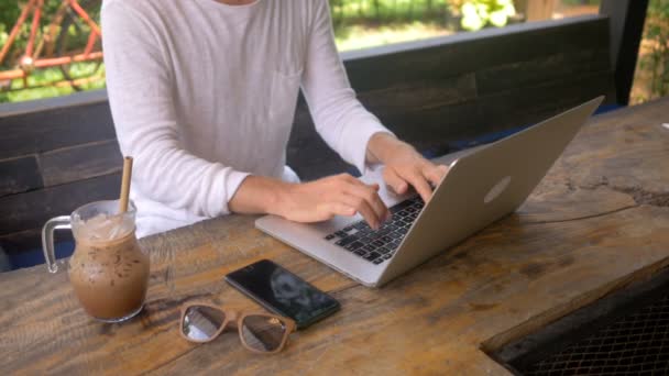 Νεαρός άνδρας ελεύθερος επαγγελματίας εργάζεται σε ένα φορητό υπολογιστή σε εξωτερική καφετέρια — Αρχείο Βίντεο