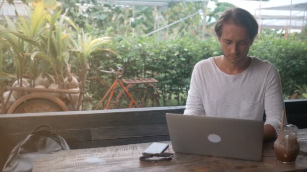 Joven freelancer trabajando en un ordenador portátil en una cafetería al aire libre — Vídeos de Stock