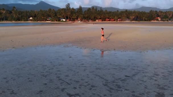 A young woman jogging at the beach on sunset. aerial drone shot, slow motion — Stock Video