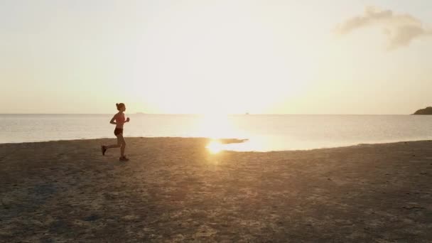 Молода жінка біжить на пляжі на заході сонця. повітряний дрон постріл, повільний рух — стокове відео