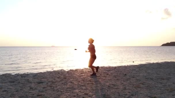 Egy fiatal nő, a naplemente a strandon kocogás. légi drone lövés, lassú mozgás — Stock videók