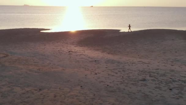 Młoda kobieta, jogging na plaży na zachód słońca. drone aerial strzał, zwolnionym tempie — Wideo stockowe