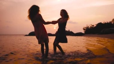 iki mutlu dans eden kız yavaş gün batımında sahilde elele