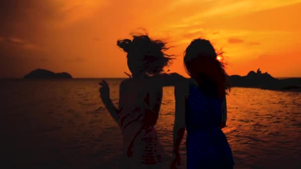 Twee gelukkige meisjes dansen op het strand bij zonsondergang in slow motion — Stockvideo