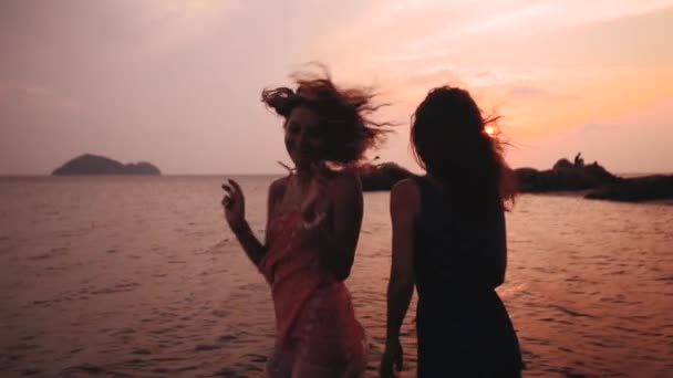 Zwei glückliche Mädchen tanzen am Strand bei Sonnenuntergang in Zeitlupe — Stockvideo