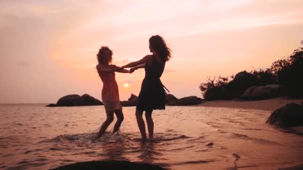 Two happy dancing girls holding hands on the beach at sunset in slow motion — Stock Video