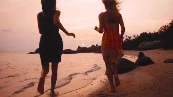 Två glada tjejer som kör i vatten vid solnedgången i slow motion — Stockvideo