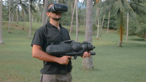 Человек с оружием играет в игру виртуальной реальности в джунглях — стоковое видео