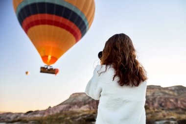 Dağın tepesinde beyaz kazak giyen turist bir fotoğrafçı kız harika manzaranın tadını çıkarıyor ve Kapadokya 'da balonların fotoğrafını çekiyor. Türkiye 'de seyahat fotoğrafçısı