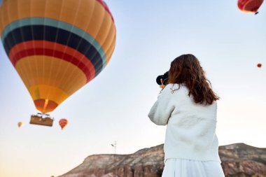 Dağın tepesinde beyaz kazak giyen turist bir fotoğrafçı kız harika manzaranın tadını çıkarıyor ve Kapadokya 'da balonların fotoğrafını çekiyor. Türkiye 'de seyahat fotoğrafçısı