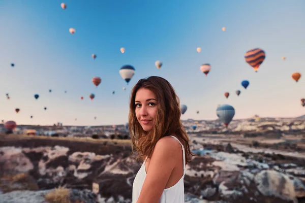 A tourist girl wearing white sweater on a mountain top enjoying wonderful view of balloons in Cappadocia. Happy Travel in Turkey concept — Stock Photo, Image