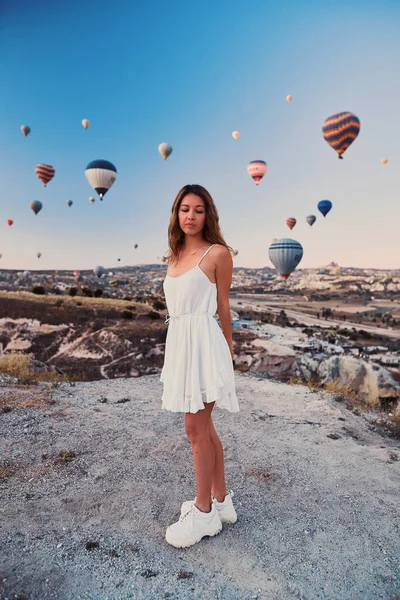 En turist flicka bär vit tröja på en bergstopp njuter av underbar utsikt över ballonger i Kappadokien. Happy Travel i Turkiet-konceptet — Stockfoto