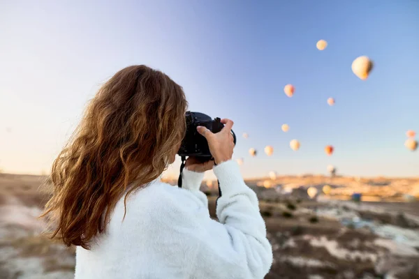 Une photographe touristique portant un pull blanc sur un sommet de montagne profitant d'une vue magnifique et prenant des photos de ballons en Cappadoce. Photographe de voyage en Turquie — Photo