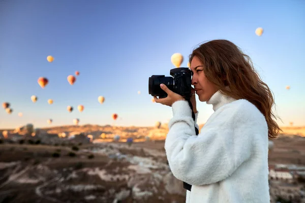 Une photographe touristique portant un pull blanc sur un sommet de montagne profitant d'une vue magnifique et prenant des photos de ballons en Cappadoce. Photographe de voyage en Turquie — Photo