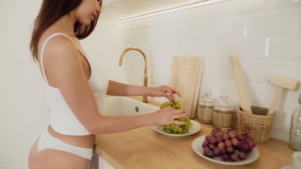 Bella donna sexy in lingerie bianca Washing Grape. Mano che tiene l'uva fresca sotto l'acqua corrente nel lavandino della cucina al rallentatore . — Video Stock