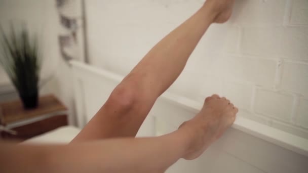 Женские ноги на кровати в белом постельном белье — стоковое видео