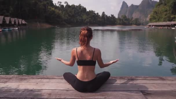 Vrouw die aan het meer zit en yoga beoefent — Stockvideo