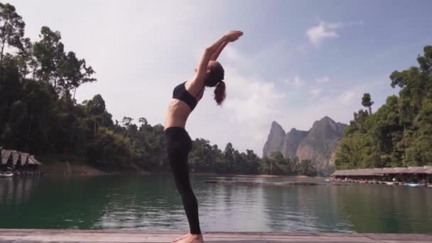 Egy nő ül a tónál és jógázik. — Stock videók