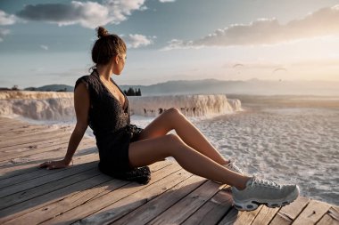 Siyah elbiseli genç seksi kız Pamukkale havuzunda oturuyor.