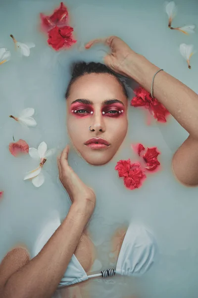 Модный портрет красивой женщины с красными и белыми цветами в ванне с молоком — стоковое фото