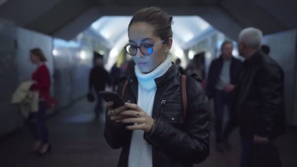 Mujer de pie en la entrada de una estación de metro utilizando un teléfono inteligente — Vídeos de Stock