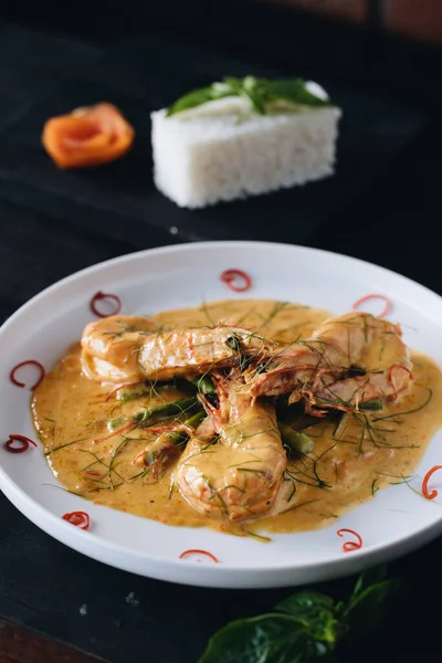 Prawns in Curry sauce on white plate on black wooden background