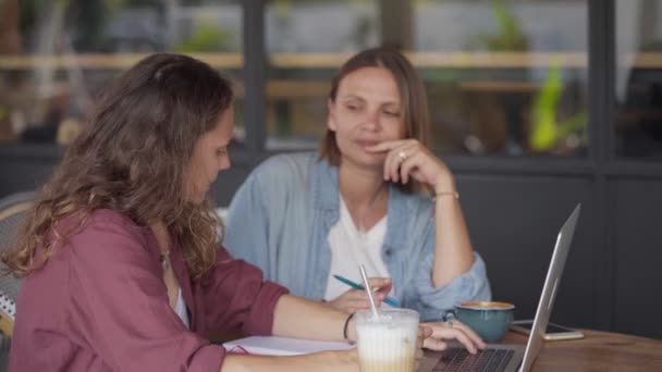 Ευτυχισμένες φίλες που δουλεύουν μαζί με το laptop στο υπαίθριο καφέ — Αρχείο Βίντεο