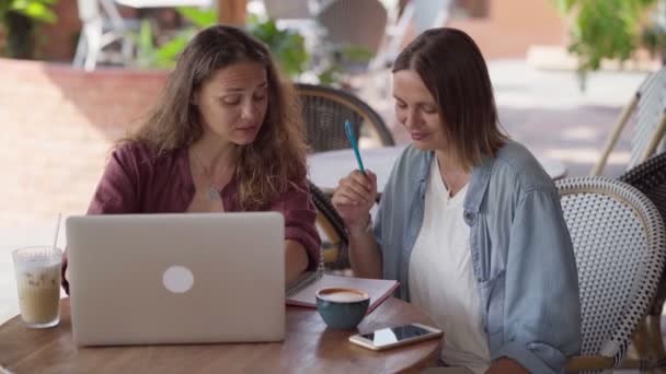 Šťastné přítelkyně pracující společně s notebookem v venkovní kavárně — Stock video