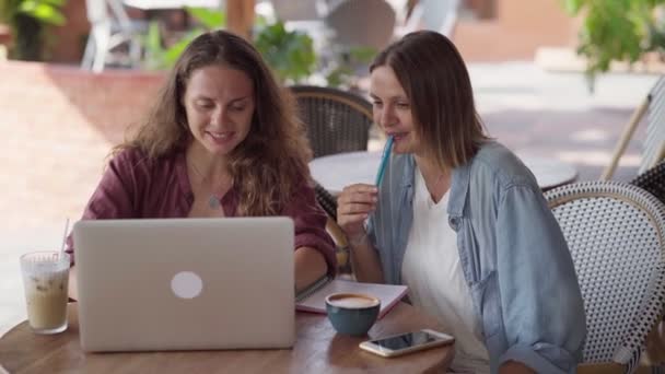 Gelukkig vrouwelijke vrienden werken samen met laptop in outdoor cafe — Stockvideo