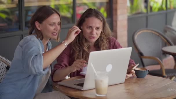 Glada kvinnor arbetar tillsammans med bärbar dator på uteservering — Stockvideo