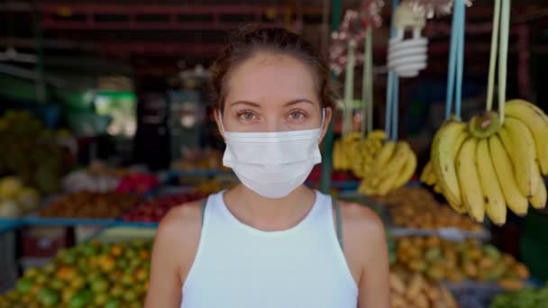 Jeune femme portant un masque de protection debout dans le marché et regarder la caméra — Video