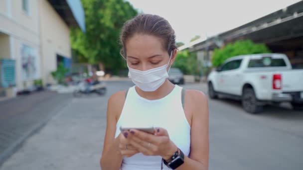 Jonge vrouw draagt een beschermend masker op straat en gebruikt haar mobiele telefoon — Stockvideo
