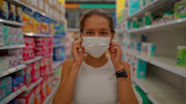 Młoda kobieta zużywa maskę ochronną stojąc w sklepie, patrząc w obiektyw i uśmiechając się — Wideo stockowe