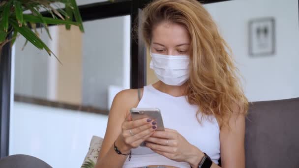 Mladá žena nosí bílou ochrannou masku používat smartphone — Stock video