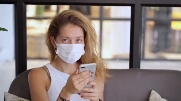 Jonge vrouw met wit beschermend masker smartphone gebruiken — Stockvideo