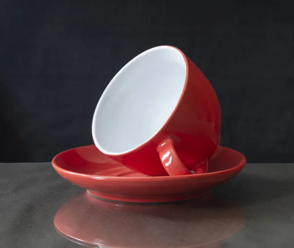 Красная чашка лежит в блюдце на столе — стоковое фото