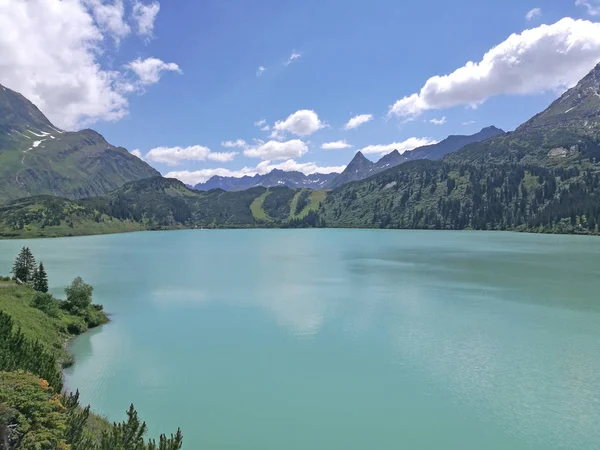 在照片的前景中 是被奥地利阿尔卑斯山环绕的绿松石水的科普斯湖 这是一个阳光灿烂的日子 白云稀少 奥地利福拉尔贝格联邦州的景观 — 图库照片