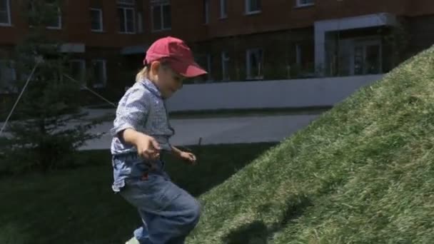 Un niñito macho corre y se dirige a la colina y se acerca — Vídeos de Stock