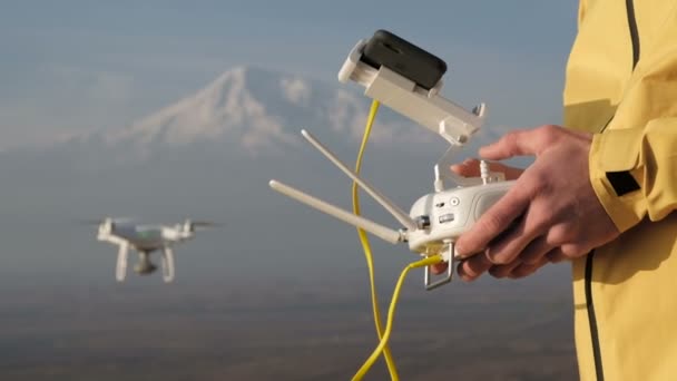 Mannen händerna styra flygande quadcopter nära mountain — Stockvideo