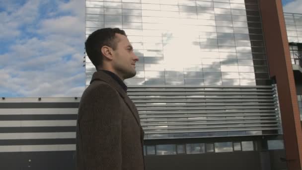 Модный бизнесмен в пальто проходит мимо здания стеклянного офиса крупным планом — стоковое видео