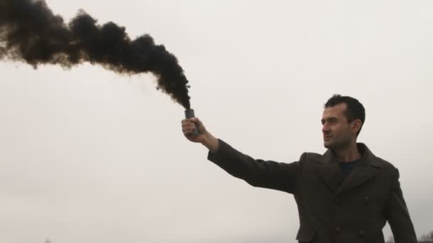 Un homme sérieux tenant une bombe à fumée avec de la fumée noire — Video