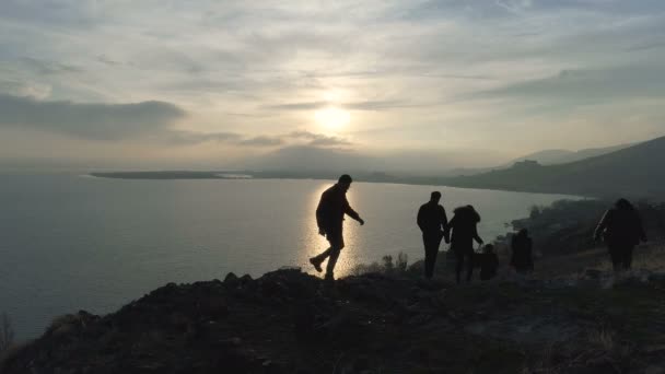 Друзі, що йдуть на схилі заходу сонця до озера — стокове відео