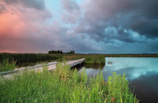 Stormachtige zonsondergang op de rivier met brug — Stockfoto