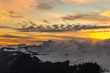 Karlı dağlar üzerinden canlı turuncu günbatımı