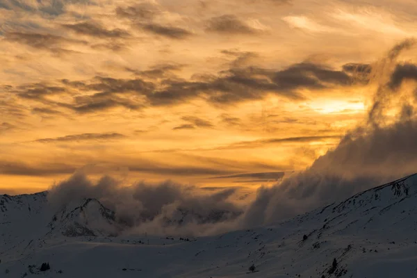 Яскравий помаранчевий захід сонця над засніженими горами — стокове фото