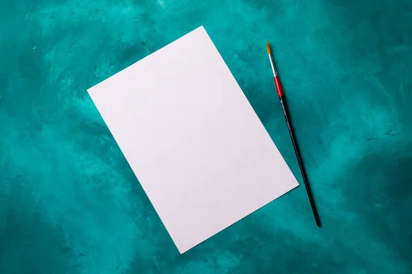 Clear white paper sheet with brush lies on turquoise background.