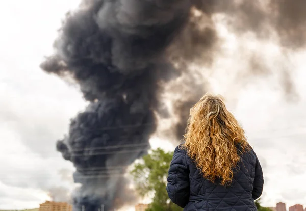 A woman observes a column of smoke flooding the sky of a populat — Stock Photo, Image