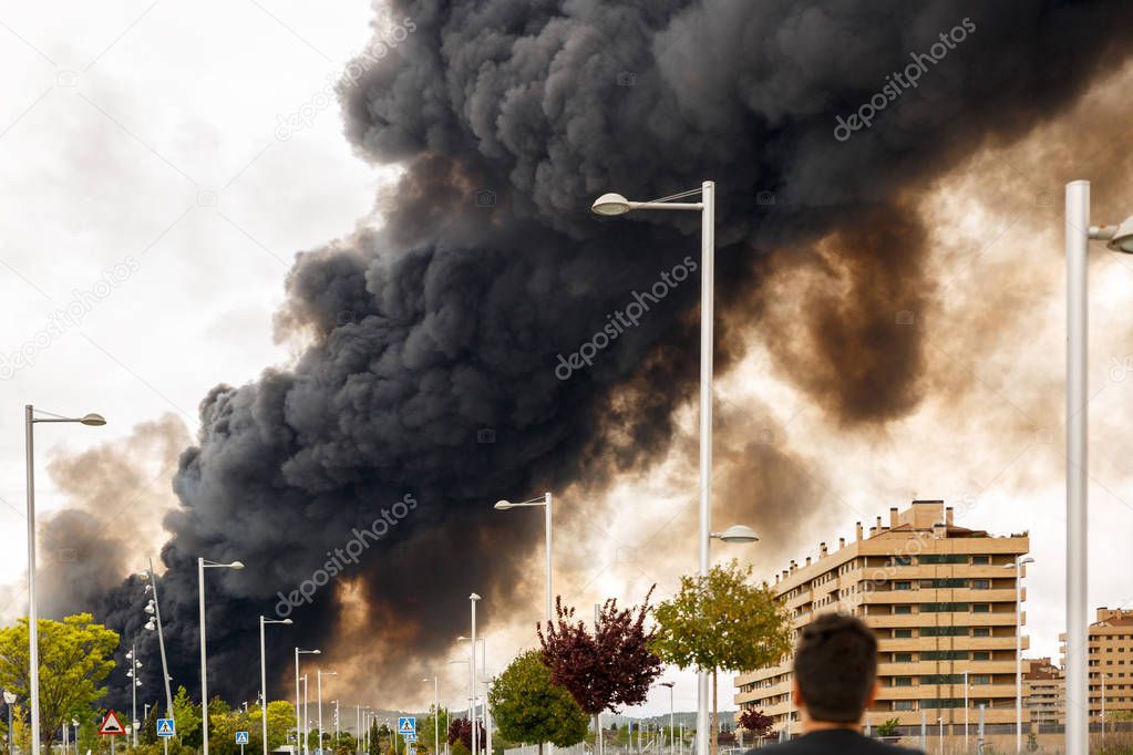 A man observes a dense and dark smoke from a fire
