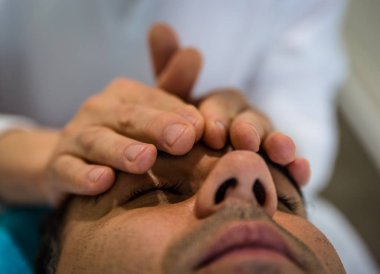 Bir terapist ellerini bir adamın alnına koyar.